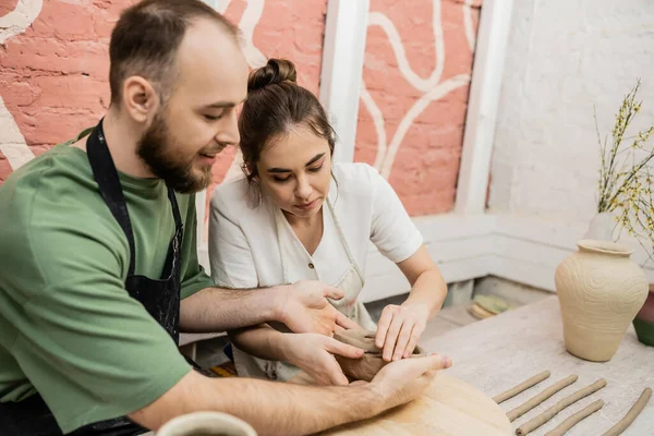 Romantic couple of artisans in aprons shaping earthenware in ceramic workshop — Stock Photo