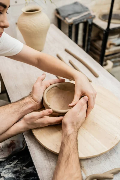 Cropped view of craftswoman making clay bowl with boyfriend in ceramic workshop — Stock Photo
