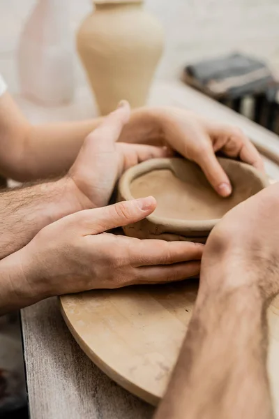 Cropped view of couple of artisan shaping clay bowl near table in ceramic workshop — Stock Photo