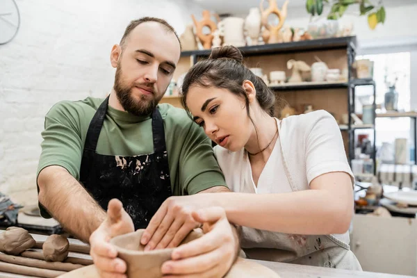 Artesanal em avental moldando tigela de barro com namorado e falando enquanto trabalhava em oficina de cerâmica — Fotografia de Stock