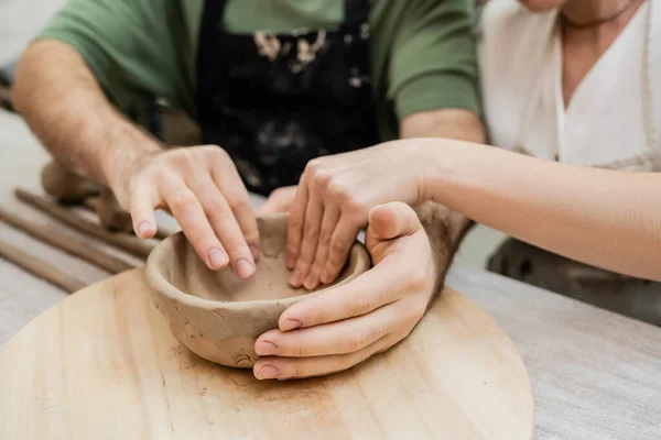 Cropped view of blurred couple of sculptors shaping clay bowl while working in ceramic studio — Stock Photo