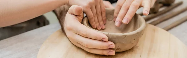 Cropped view of couple of artisan shaping clay bowl together in ceramic studio, banner — Stock Photo