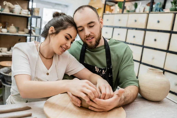 Positive romantic couple of potters making clay bowl in ceramic workshop at background — Stock Photo