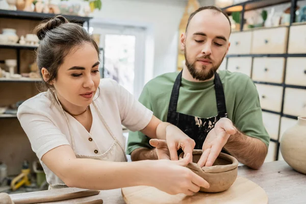 Artesana en delantal confeccionando tazón de barro con novio juntos en taller de cerámica - foto de stock