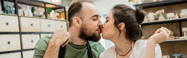 Пара ремесленников в фартуках целуются, стоя в керамической мастерской на заднем плане, баннер — стоковое фото