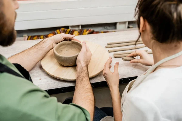 Vue recadrée de l'artisan en tablier façonnant bol d'argile près de petite amie dans l'atelier de poterie — Photo de stock