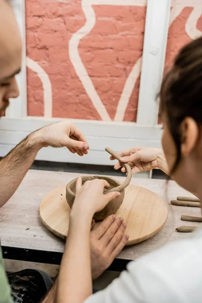 Casal desfocado de artesãos moldando tigela de barro em placa de madeira no estúdio de cerâmica no fundo — Fotografia de Stock