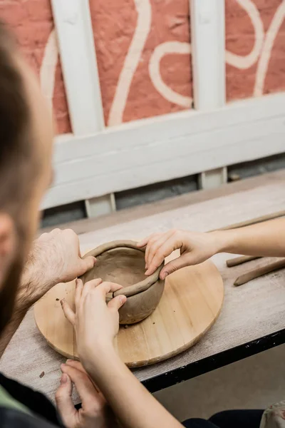 Blurred couple of potters creating clay bowl and working in ceramic workshop at background — Stock Photo