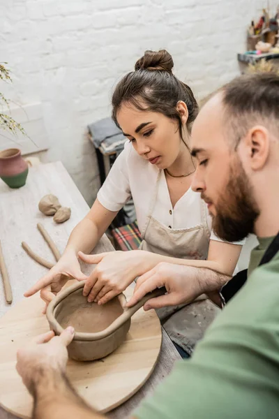 Брюнетка майстер в фартух формуючи глину з розмитим задоволеним разом в керамічній студії — стокове фото