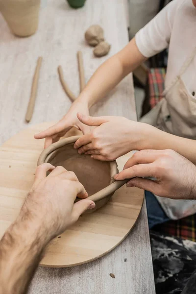 Cropped view of craftswoman creating clay bowl with boyfriend together in pottery workshop — Stock Photo