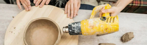 Vue du dessus des artisans séchant de la terre cuite avec pistolet à chaleur à bord dans un atelier de céramique, bannière — Photo de stock