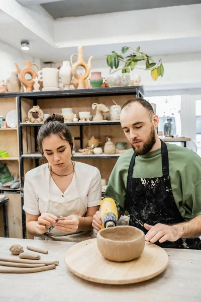 Craftsman drying earthenware with heat gun while girlfriend shaping clay in ceramic workshop — Stock Photo