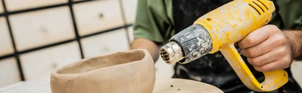 Vista cortada da tigela de argila de secagem de oleiro com pistola de calor em placa de madeira na oficina de cerâmica, banner — Fotografia de Stock