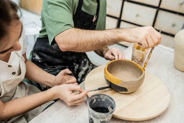 Craftswoman in apron coloring clay bowl with boyfriend together in ceramic workshop — Stock Photo