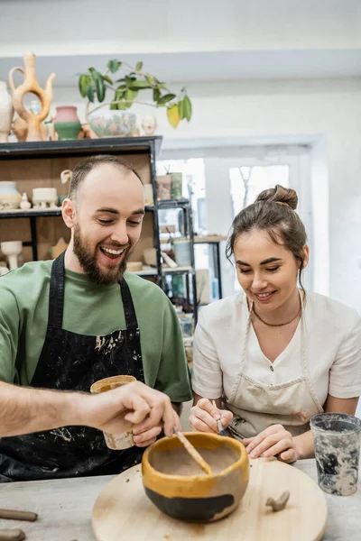 Positive romantic couple of artisans coloring clay eathenware together in ceramic workshop — Stock Photo