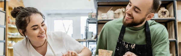 Joyful potters in aprons dying clay bowl together while working in pottery studio at background — Stock Photo