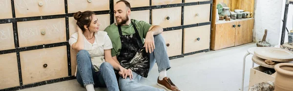 Couple souriant de sculpteurs assis sur le sol près du placard dans un atelier de céramique, bannière — Photo de stock