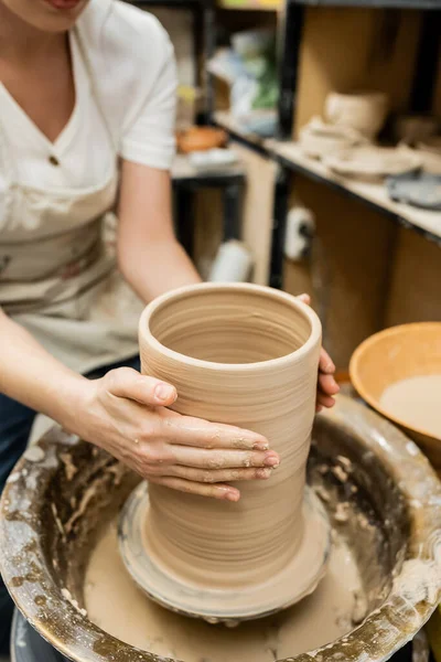Vista cortada de oleiro fêmea esculpir argila na roda de cerâmica em oficina de cerâmica turva — Fotografia de Stock