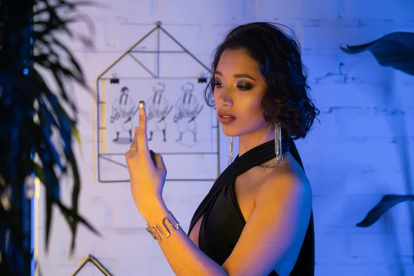 Stylish young asian woman in dress taking selfie on smartphone in night club with neon light — Stock Photo