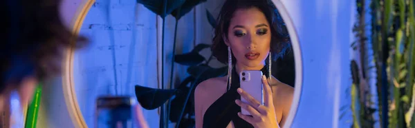 Moda joven asiático mujer tomando selfie en smartphone cerca espejo y plantas en night club, banner - foto de stock