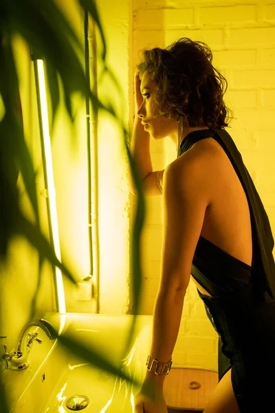 Seitenansicht einer stilvollen und eleganten asiatischen Frau, die in der Nähe von Waschbecken und Leuchtstofflampe im Nachtclub steht — Stockfoto