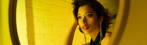 Elegante joven mujer asiática con maquillaje mirando el espejo en luz de neón en el club nocturno, pancarta - foto de stock