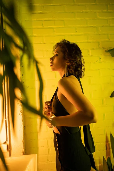 Вид сбоку на элегантную женщину, трогающую платье, стоя в желтом неоновом свете в ночном клубе — стоковое фото