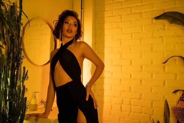Модная молодая азиатка в сексуальном платье, стоящая возле раковины и неонового освещения в ночном клубе — стоковое фото