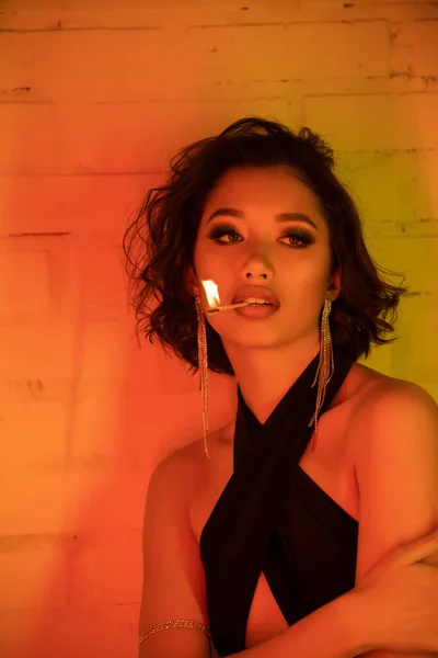 Trendy giovane donna asiatica in abito tenuta partita con il fuoco in labbra in night club con luce al neon — Foto stock
