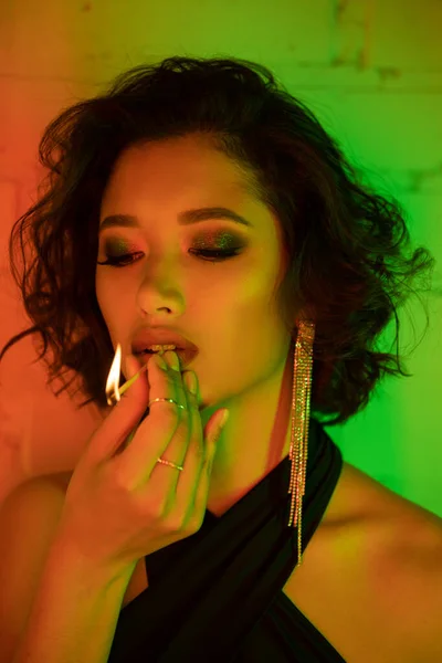 Portrait of stylish asian woman holding match with fire while standing in night club with neon light — Stock Photo