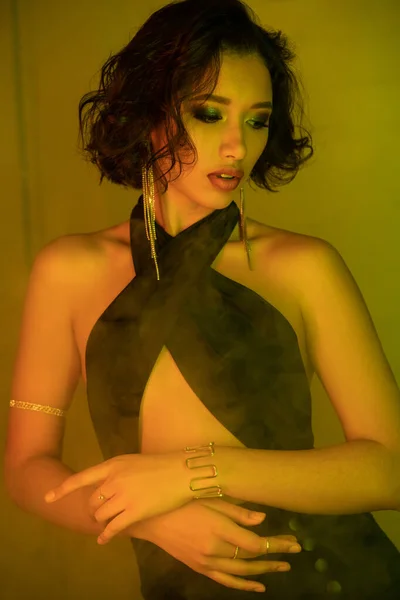 Елегантна азіатка в сережках і сукні стоїть в диму і неоновому світлі в нічному клубі — стокове фото