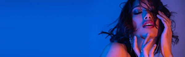 Glamours jeune femme asiatique touchant le visage tout en posant dans la lumière au néon dans la boîte de nuit, bannière — Photo de stock
