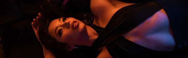 Draufsicht auf elegante junge asiatische Frau, die im Nachtclub auf der Couch im Neonlicht liegt, Banner — Stockfoto