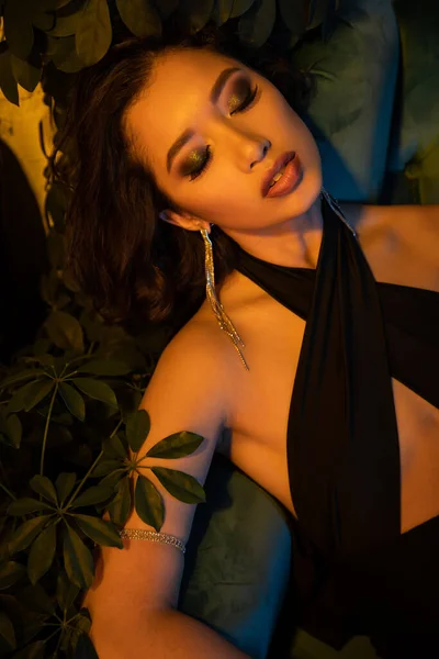 Moda joven asiática mujer en traje de noche sentado en sillón en club nocturno con iluminación - foto de stock
