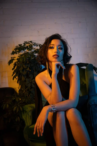 Elegante giovane donna asiatica con trucco e acconciatura seduta su poltrona nel night club — Foto stock