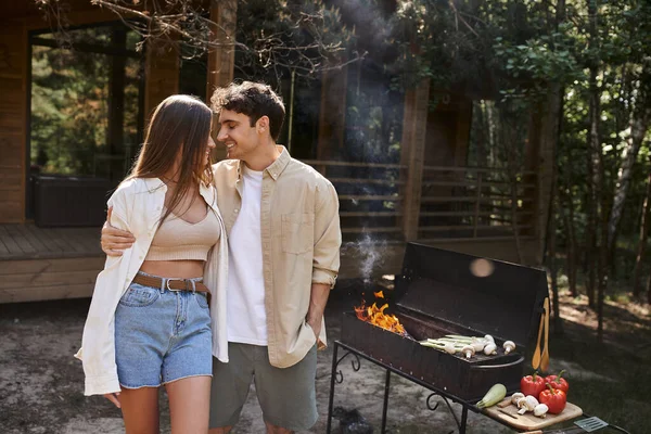 Homme heureux étreignant petite amie près du barbecue grill, romance d'été, couple, maison de vacances — Photo de stock