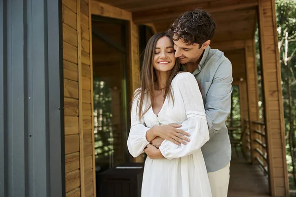Homme heureux étreignant petite amie en robe de soleil blanche près de la maison de vacances, été, escapade romantique — Photo de stock