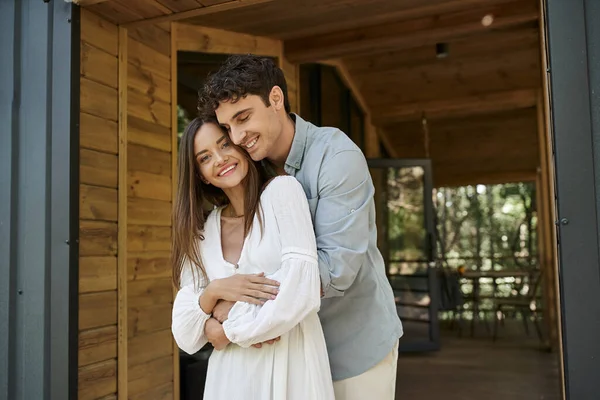 Glücklicher Mann umarmt schöne Frau in weißer Kleidung in der Nähe von Ferienhaus, Sommer, romantisches Wochenende — Stockfoto