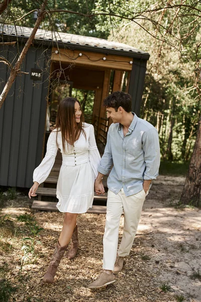 Homem positivo e mulher de mãos dadas e caminhando juntos perto da casa de verão, férias, romance — Fotografia de Stock
