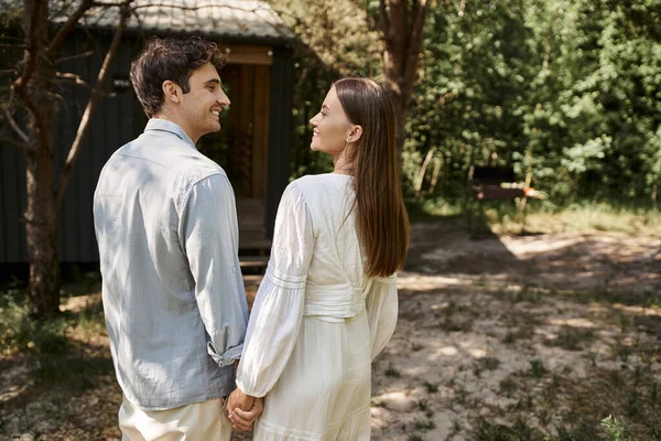 Hombre y mujer felices en vestido blanco tomados de la mano, mirándose, escapada de verano, romance - foto de stock