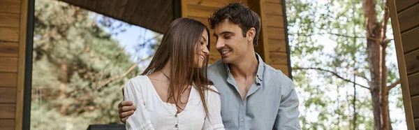 Pancarta, hombre feliz abrazando a la mujer alegre mientras está sentado en el porche, pareja romántica, casa de vacaciones - foto de stock