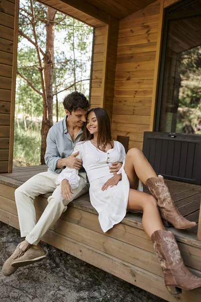 Romantischer Mann umarmt fröhliche Frau, während sie zusammen auf der Veranda sitzt, Paar, Ferienhaus, Urlaub — Stockfoto