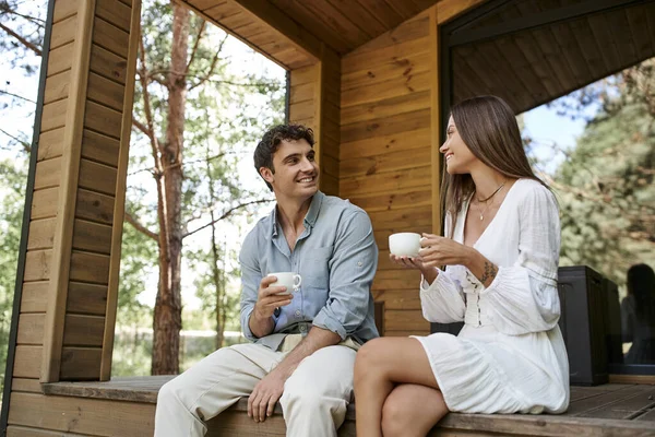 Romantic getaway, man and woman holding cups of morning coffee, couple on porch of vacation house — Stock Photo