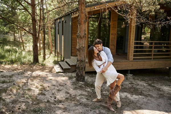 Hombre abrazando mujer cerca de casa de vacaciones, en el bosque, el verano y el romance, la felicidad y la risa - foto de stock