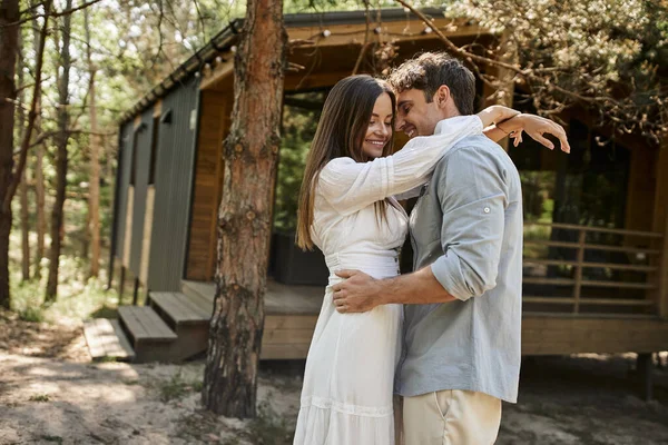 Летняя радость, счастливая женщина с татуировкой на руке обнимается с парнем возле домика отдыха в лесу — стоковое фото