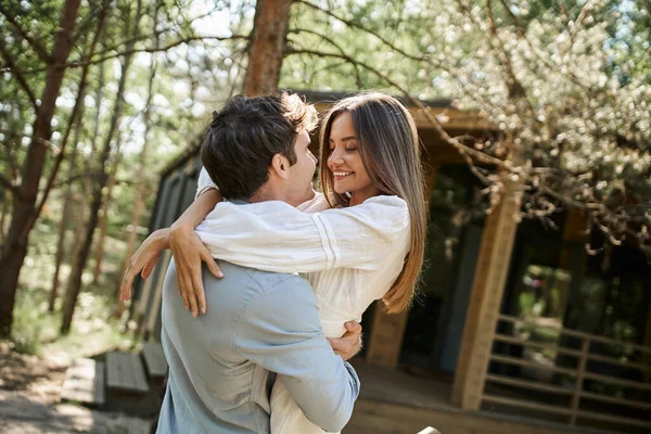 Homme et femme heureux étreignant et se regardant, maison de vacances dans la forêt, romance et amour — Photo de stock