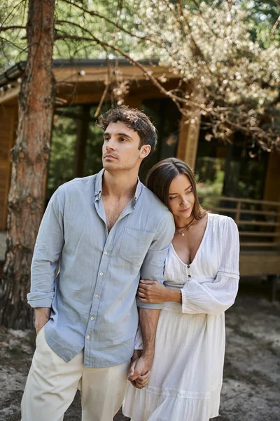 Femme en robe blanche tenant la main avec petit ami, debout près de la maison d'été, vacances, romance — Photo de stock