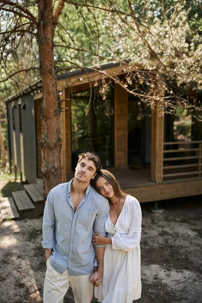 Woman in white sundress holding hands with boyfriend, looking at camera near summer house, romance — Stock Photo
