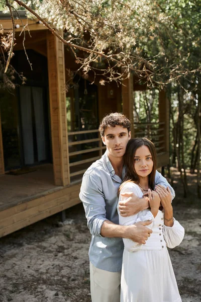 Handsome man hugging beautiful woman, couple standing near vacation house, people and nature — Stock Photo