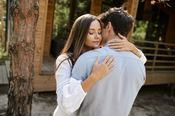 Brunette woman in sundress hugging boyfriend while standing near blurred vacation house outdoors — Stock Photo